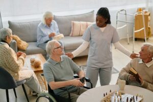 Two older adults sharing coffee and conversation in a cozy living room with plenty of natural light and personal decor.