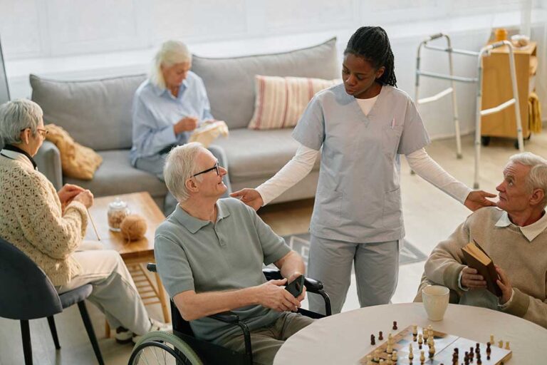 Two older adults sharing coffee and conversation in a cozy living room with plenty of natural light and personal decor.